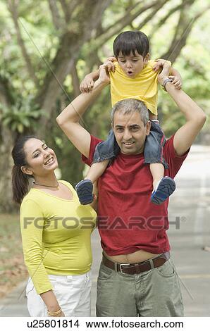 Mid adult man carrying his son on his shoulder with his wife standing beside him View Large Photo Image Picture - Mid adult man carrying his son on his shoulder with his wife standing beside him. Fotosearch