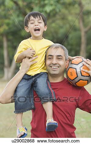 Stock Photo - Mid adult man carrying his son on his shoulder and holding a soccer ball. Fotosearch