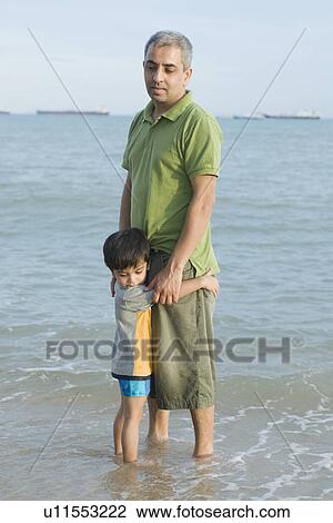 Stock Image - Mid adult man standing with his son on the beach . Fotosearch