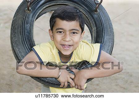 Stock Image - Portrait of a boy playing on a tire swing. Fotosearch