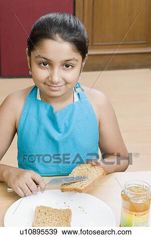 Portrait of a girl spreading jam on a bread slice View Large Photo Image Stock Photo - Portrait of a girl spreading jam on a bread slice. Fotosearch