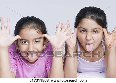 Stock Photo - Portrait of two girls making their faces with sticking their tongues out. Fotosearch