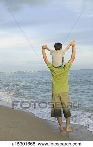 Stock Photo - Rear view of a mid adult man carrying his son on his shoulders. Fotosearch