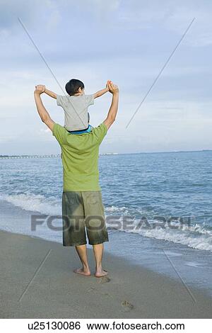 Rear view of a mid adult man carrying his son on his shoulders View Large Photo Image Stock Photograph - Rear view of a mid adult man carrying his son on his shoulders . Fotosearch