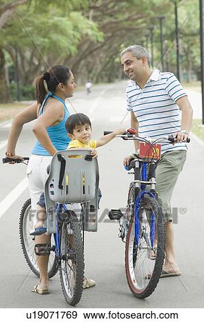 Side profile of a mid adult couple talking to each other with their son riding a bicycle View Large Photo Image Stock Photo - Side profile of a mid adult couple talking to each other with their son riding a bicycle. Fotosearch