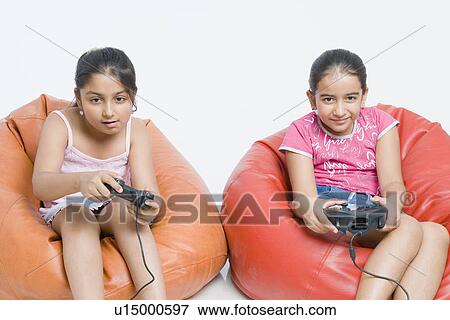 Two girls sitting on bean bags and playing a video game View Large Photo Image Stock Photo - Two girls sitting on bean bags and playing a video game. Fotosearch