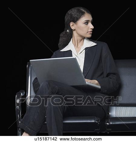 Businesswoman sitting on a bench and using a laptop View Large Photo Image Stock Image - Businesswoman sitting on a bench and using a laptop. Fotosearch