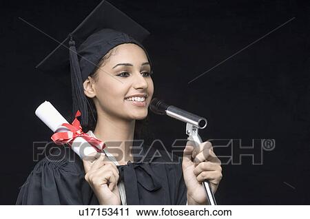 Stock Image - Close-up of a young female graduate holding a diploma and speaking on a microphone. Fotosearch