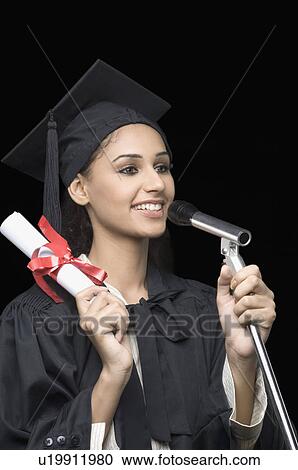 Stock Image - Close-up of a young female graduate holding a diploma and giving a speech. Fotosearch