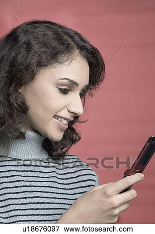 Close-up of a young woman holding a mobile phone and smiling View Large Photo Image Stock Photo - Close-up of a young woman holding a mobile phone and smiling. Fotosearch