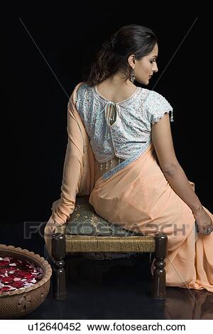 Rear view of a mid adult woman in lehenga choli and sitting on a stool with a bowl of petals View Large Photo Image Stock Image - Rear view of a mid adult woman in lehenga choli and sitting on a stool with a bowl of petals. Fotosearch