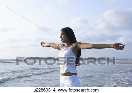 Side profile of a young woman standing with arm outstretched on the beach View Large Photo Image Picture - Side profile of a young woman standing with arm outstretched on the beach. Fotosearch