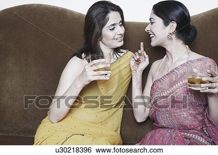 Stock Photograph - Two young women sitting on a couch holding glasses of whiskey. Fotosearch