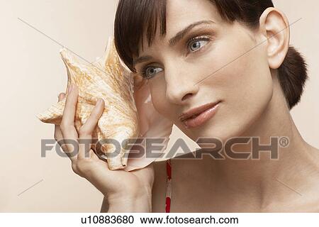 Mid adult woman holding conch shell to ear View Large Photo Image Stock Image - Mid adult woman holding conch shell to ear. Fotosearch