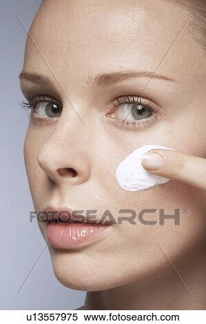 Stock Photography - Young woman applying moisturizer on face. Fotosearch