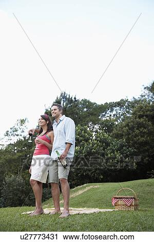 Stock Image - Couple drinking red wine and looking at view in park. Fotosearch