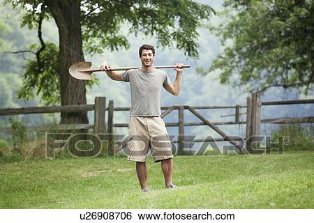 Stock Photograph - Gardener with spade standing near wooden fence. Fotosearch