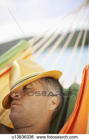 Stock Photograph - Mid adult man with hat sleeping on hammock. Fotosearch