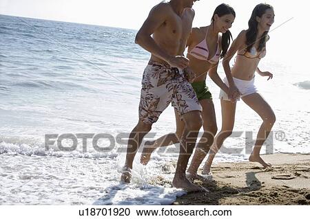Stock Image - Young adult people having fun on beach, Side View. Fotosearch