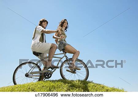 Young couple cycling on hill (low angle view) View Large Photo Image Stock Photograph - Young couple cycling on hill (low angle view). Fotosearch