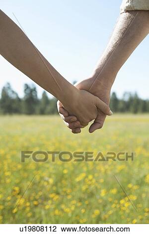 Stock Image - Young couple holding hands in a field of wildflowers (focus on hands). Fotosearch