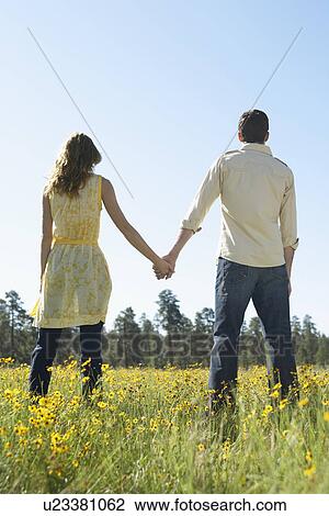 Stock Image - Young couple holding hands in a field of wildflowers. Fotosearch