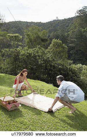 Young couple laying picnic blanket on lawn View Large Photo Image Stock Image - Young couple laying picnic blanket on lawn. Fotosearch