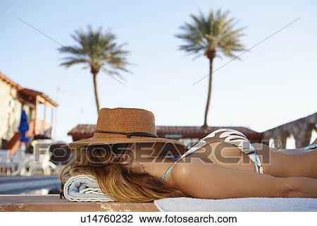 Stock Image - Woman sleeping with hat on her face at poolside. Fotosearch