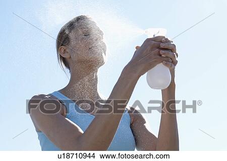 Woman spraying water on face (low angle view) View Large Photo Image Picture - Woman spraying water on face (low angle view). Fotosearch