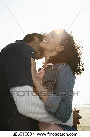 Young couple hugging on beach (lens flare) View Large Photo Image Stock Photo - Young couple hugging on beach (lens flare). Fotosearch