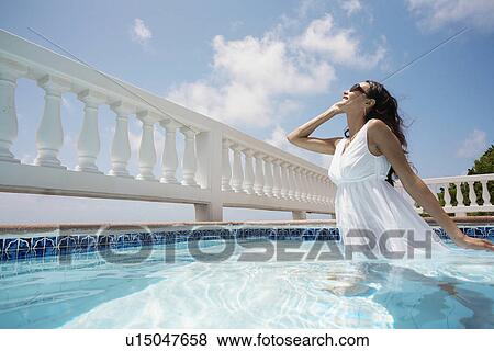 Stock Photo - Young woman wearing dress in swimming pool. Fotosearch