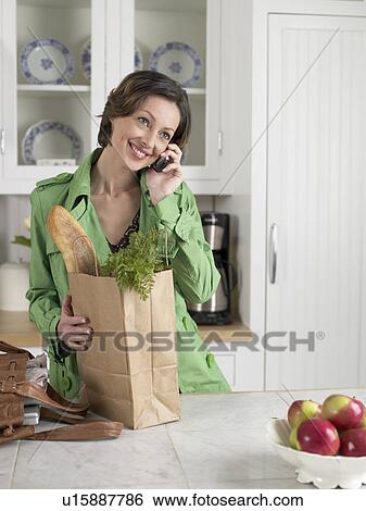 Stock Photograph - Mid adult woman with bag of groceries talking on phone. Fotosearch
