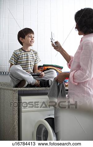 Mother photographing son in laundry room View Large Photo Image Stock Image - Mother photographing son in laundry room. Fotosearch