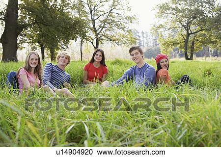 Stock Image - Five teenagers sitting in field (portrait). Fotosearch