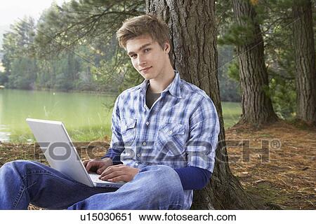 Teenage boy using laptop at lakeside View Large Photo Image Stock Image - Teenage boy using laptop at lakeside. Fotosearch