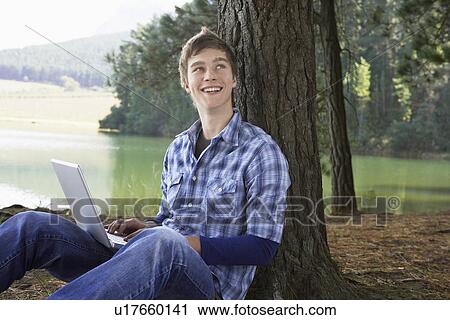Teenage boy using laptop at lakeside View Large Photo Image Stock Image - Teenage boy using laptop at lakeside. Fotosearch