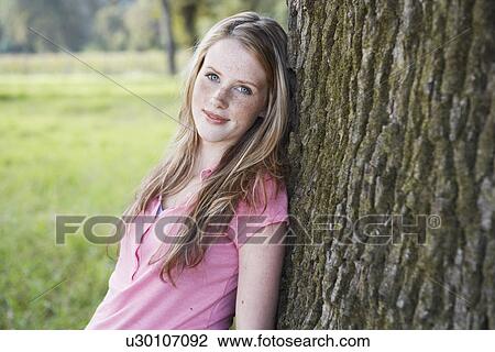 Teenage girl leaning on tree trunk (portrait) View Large Photo Image Stock Image - Teenage girl leaning on tree trunk (portrait). Fotosearch