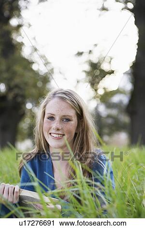 Stock Image - Teenage girl reading book in field. Fotosearch