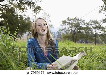 Stock Image - Teenage girl reading book in field. Fotosearch