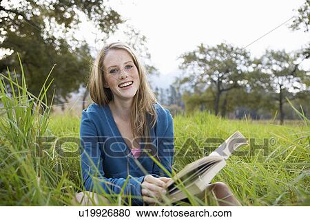Stock Image - Teenage girl reading book in field. Fotosearch