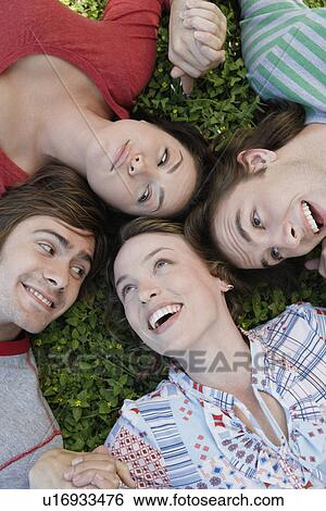 Stock Photograph - Four friends lying on grass (directly above). Fotosearch