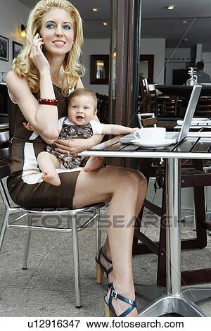 Stock Photo - Mid adult mother talking on cell phone and holding baby girl. Fotosearch