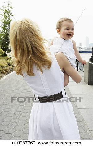 Stock Image - Mother carrying baby girl (rear view). Fotosearch