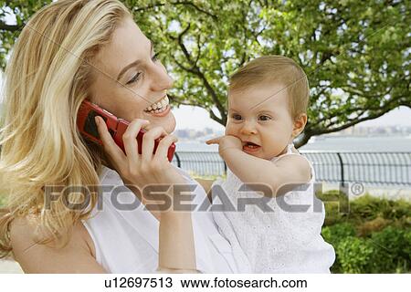 Stock Image - Mother with baby girl talking on cell phone. Fotosearch