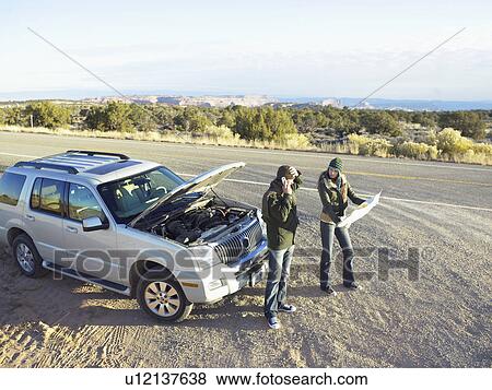 Stock Photo - Couple with broken car on roadside, man on the phone and woman with roadmap, high angle view. Fotosearch
