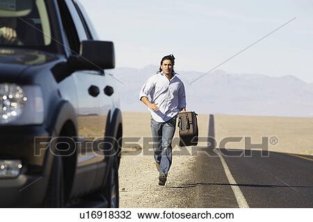 Stock Image - Male hitchhiker running towards car. Fotosearch