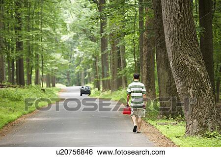 Stock Photograph - Man carrying gas canister, car out of gas in background (rear view). Fotosearch