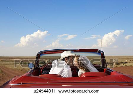 Stock Image - Newlyweds kissing in convertible. Fotosearch
