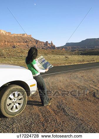 Stock Photo - Woman reading map in desert, rear view, Moab, Utah, USA. Fotosearch