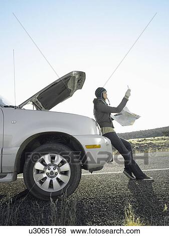 Stock Photo - Woman with road map using cell phone by broken car. Fotosearch